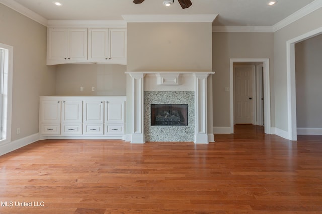 unfurnished living room featuring crown molding, ceiling fan, a premium fireplace, and light wood-type flooring