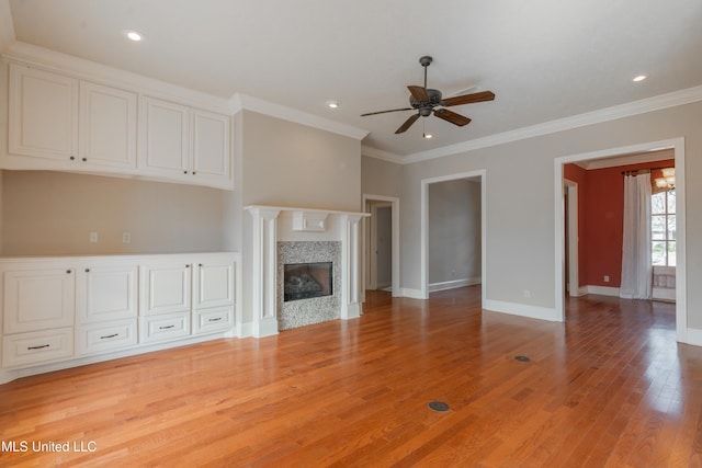 unfurnished living room with ornamental molding, a premium fireplace, ceiling fan, and light wood-type flooring