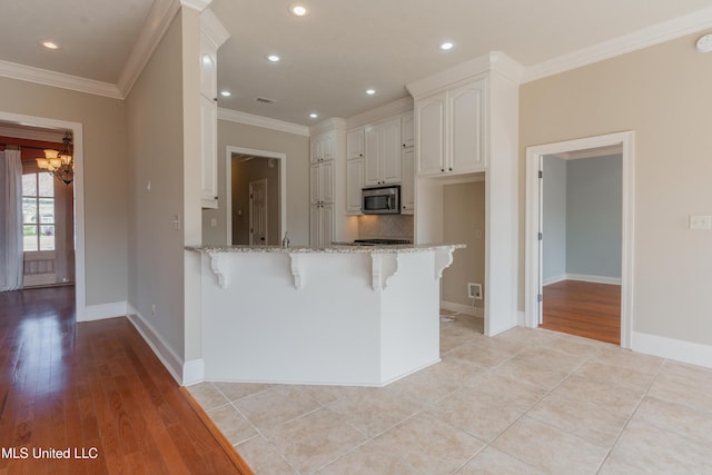 kitchen featuring a kitchen bar, white cabinetry, tasteful backsplash, light stone counters, and kitchen peninsula