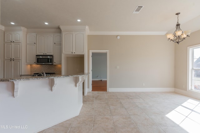 kitchen featuring a kitchen bar, white cabinetry, pendant lighting, light stone countertops, and backsplash