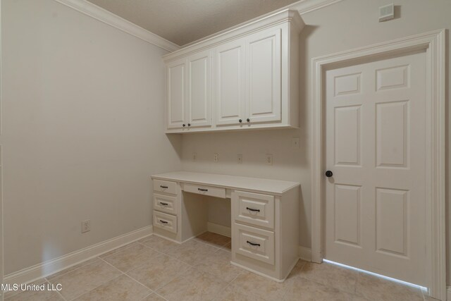 unfurnished office with crown molding, built in desk, and light tile patterned floors