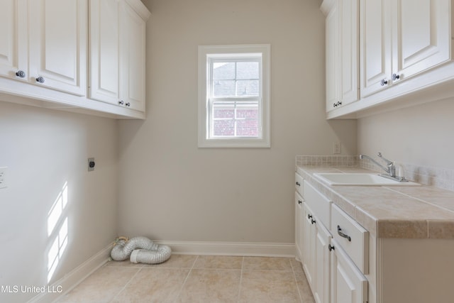 laundry area with electric dryer hookup, sink, light tile patterned floors, and cabinets