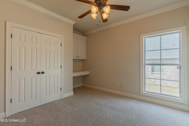 unfurnished bedroom featuring ceiling fan, built in desk, ornamental molding, light colored carpet, and a closet