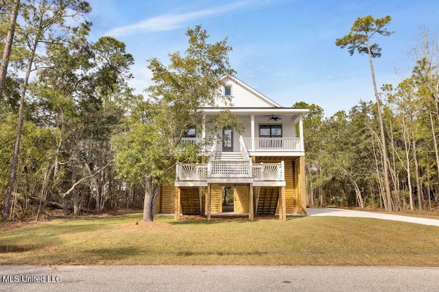 beach home featuring covered porch, stairs, a ceiling fan, and a front yard