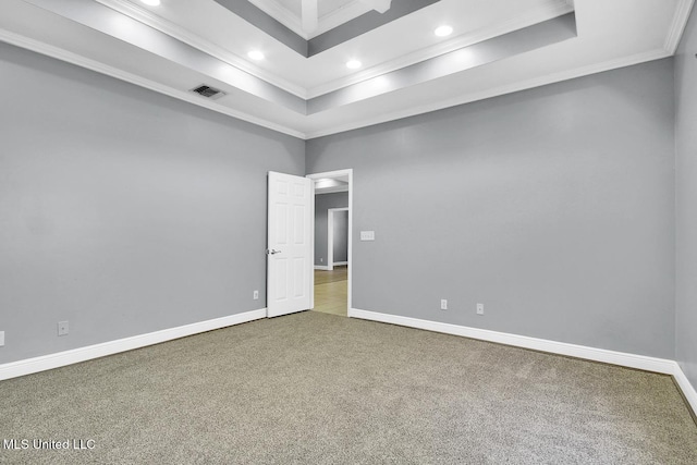 empty room with a raised ceiling, carpet, visible vents, and ornamental molding