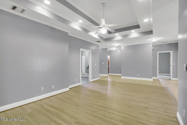 spare room with visible vents, ornamental molding, light wood-style flooring, baseboards, and a raised ceiling