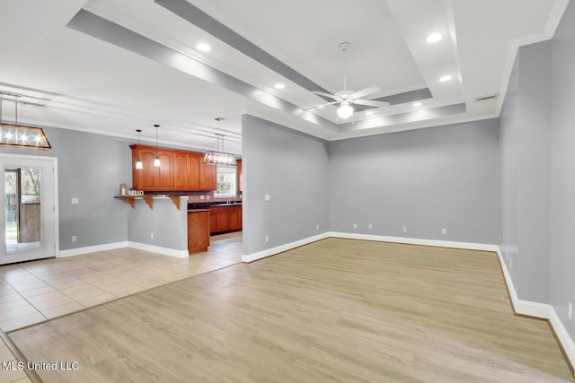 unfurnished living room with light wood finished floors, visible vents, crown molding, baseboards, and a raised ceiling