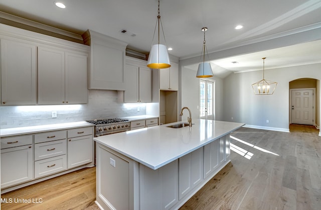 kitchen with decorative light fixtures, sink, white cabinetry, and a kitchen island with sink