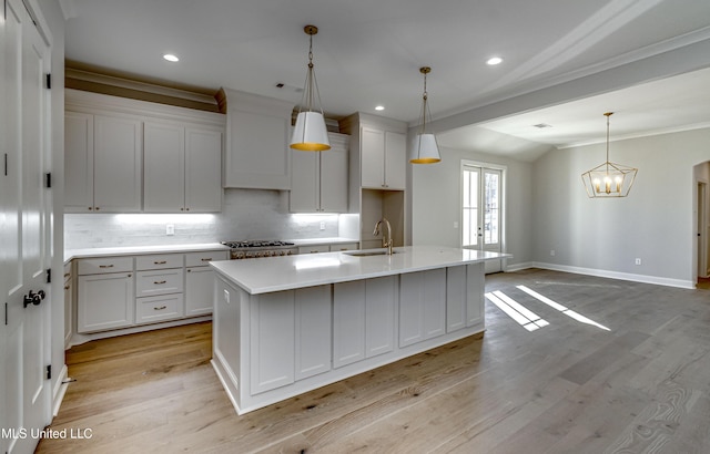 kitchen featuring range, white cabinetry, decorative backsplash, pendant lighting, and an island with sink