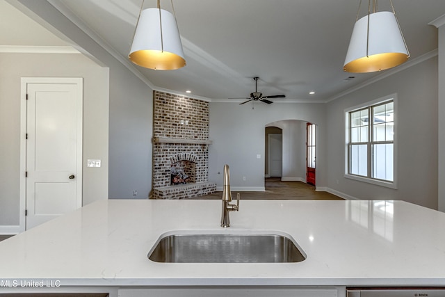 kitchen with crown molding, a fireplace, sink, decorative light fixtures, and an island with sink