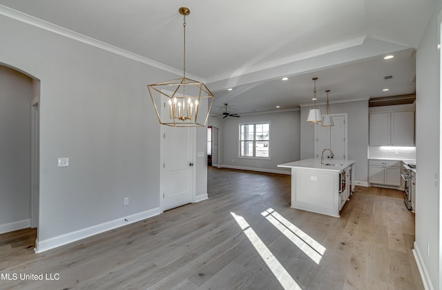 kitchen with pendant lighting, sink, white cabinets, light wood-type flooring, and a kitchen island with sink