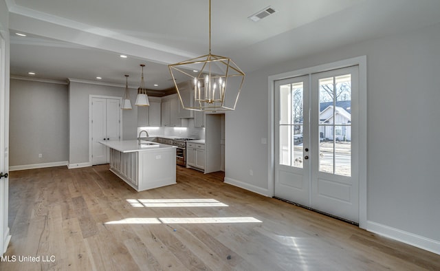 kitchen featuring pendant lighting, high end range, french doors, sink, and a kitchen island with sink