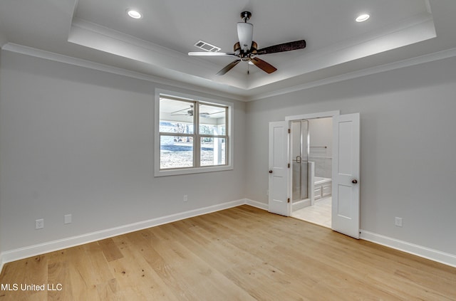 empty room with light hardwood / wood-style flooring, a tray ceiling, and ornamental molding