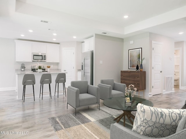 living room featuring light wood-style floors, visible vents, baseboards, and recessed lighting