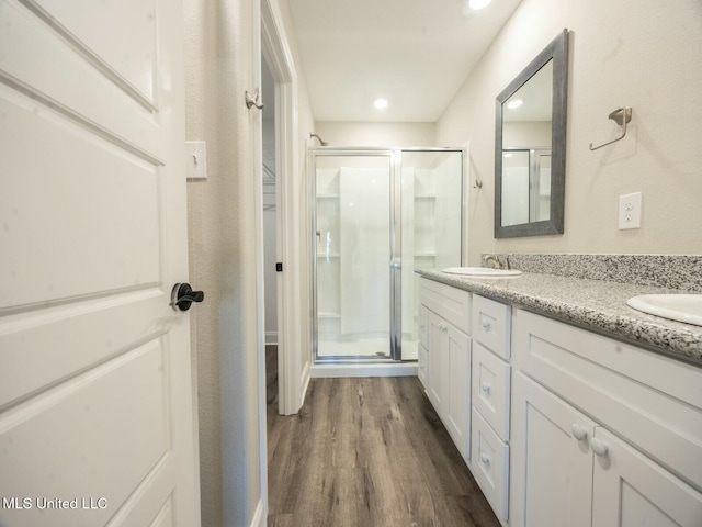 bathroom featuring double vanity, a stall shower, a sink, and wood finished floors