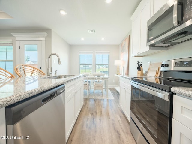 kitchen with light stone counters, appliances with stainless steel finishes, white cabinets, and a sink