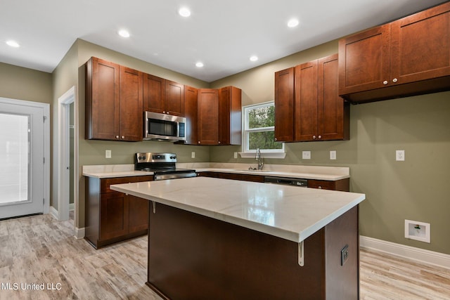 kitchen featuring light wood-style flooring, a sink, appliances with stainless steel finishes, and baseboards