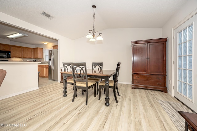 dining space with lofted ceiling, a chandelier, a textured ceiling, and light wood-type flooring