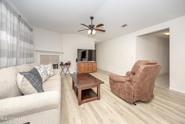 living room featuring ceiling fan, wood-type flooring, a fireplace, a textured ceiling, and vaulted ceiling