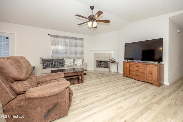 living room featuring ceiling fan, a fireplace, a textured ceiling, vaulted ceiling, and light wood-type flooring