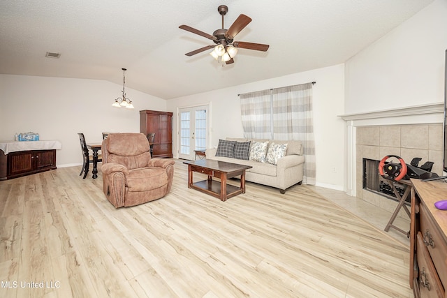 living room with vaulted ceiling, a fireplace, ceiling fan, a textured ceiling, and light hardwood / wood-style flooring