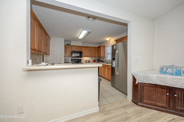 kitchen featuring electric range oven, stainless steel refrigerator with ice dispenser, light hardwood / wood-style floors, a textured ceiling, and kitchen peninsula