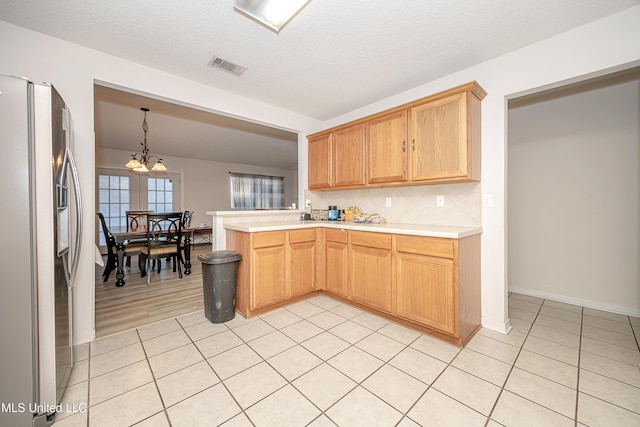 kitchen with tasteful backsplash, a chandelier, hanging light fixtures, a textured ceiling, and stainless steel fridge