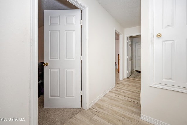 corridor with a textured ceiling and light wood-type flooring