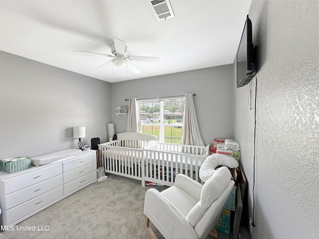 carpeted bedroom featuring a nursery area, ceiling fan, and visible vents