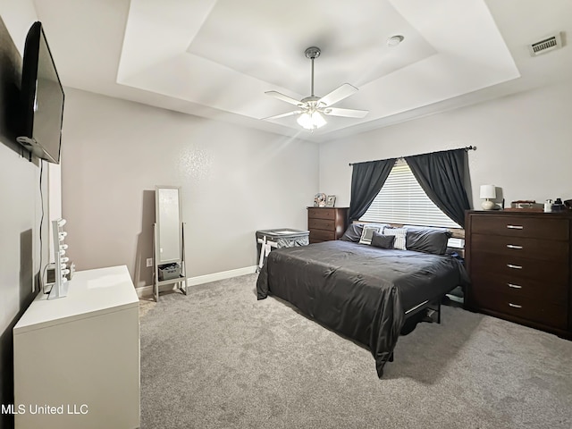 bedroom featuring light colored carpet, a ceiling fan, baseboards, a tray ceiling, and visible vents
