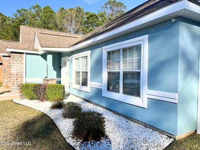 view of side of property with a shingled roof and stucco siding