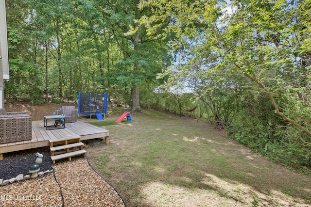view of grassy yard featuring a trampoline and a deck