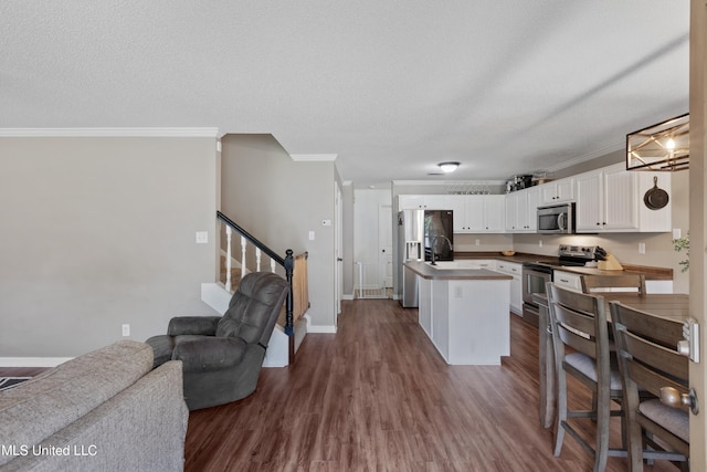 kitchen with stainless steel appliances, ornamental molding, open floor plan, white cabinetry, and an island with sink