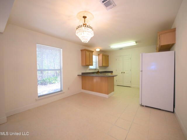 kitchen featuring a chandelier, a peninsula, freestanding refrigerator, dark countertops, and pendant lighting