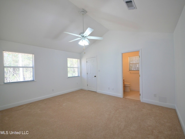 unfurnished bedroom with lofted ceiling, connected bathroom, light carpet, visible vents, and baseboards