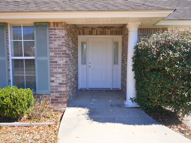 view of exterior entry featuring brick siding and roof with shingles