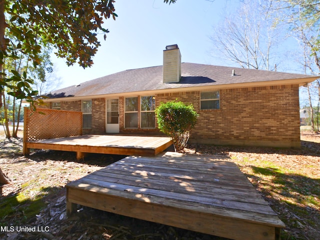 back of property featuring brick siding, a chimney, a wooden deck, and roof with shingles