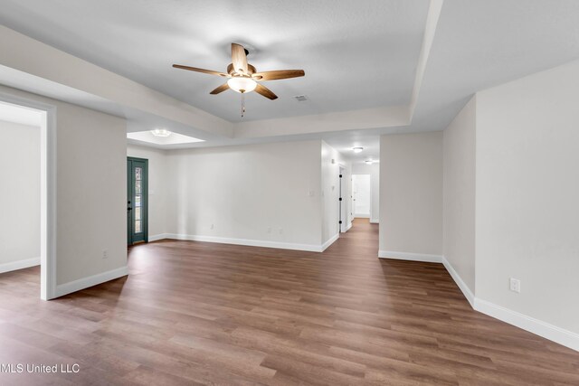 unfurnished room featuring a tray ceiling, baseboards, and wood finished floors