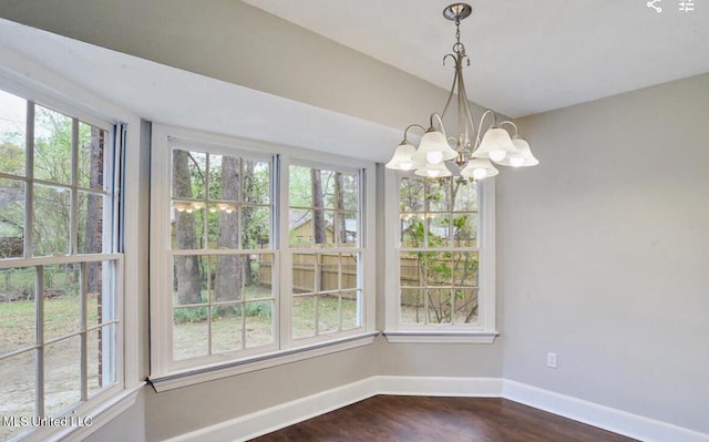 unfurnished dining area featuring a chandelier, dark wood-type flooring, and baseboards