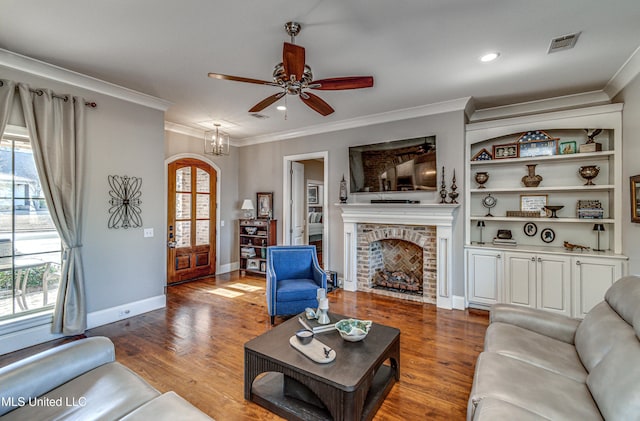 living room featuring ceiling fan with notable chandelier, wood-type flooring, built in shelves, a fireplace, and crown molding