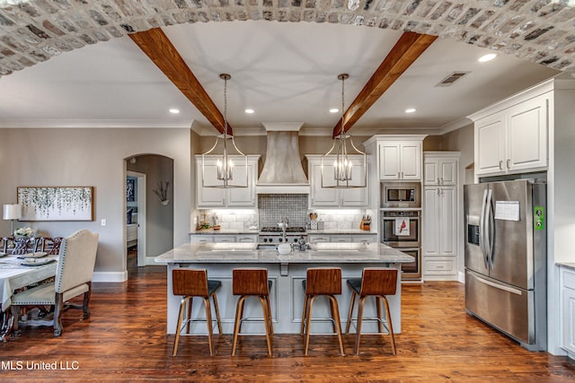 kitchen with a center island with sink, stainless steel appliances, hanging light fixtures, light stone countertops, and white cabinets