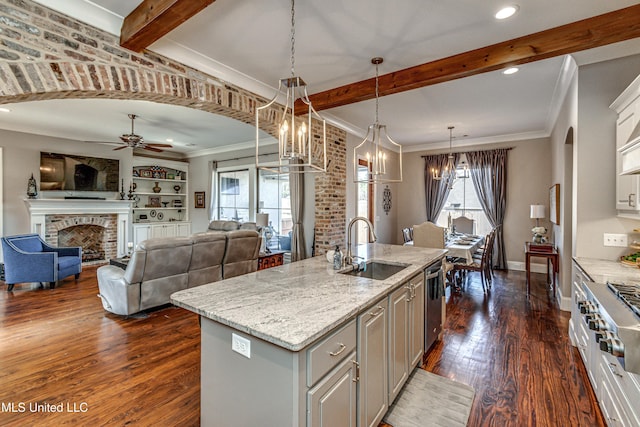 kitchen with light stone countertops, decorative light fixtures, a fireplace, an island with sink, and ceiling fan