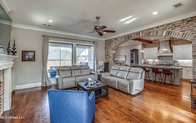 living room featuring ceiling fan, dark hardwood / wood-style floors, ornamental molding, and a brick fireplace