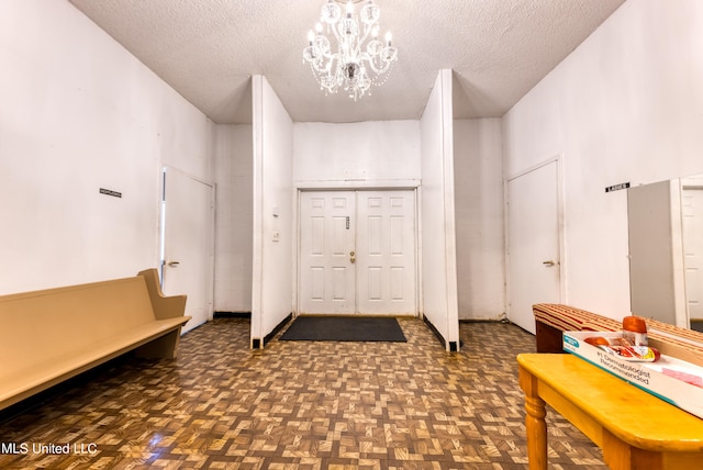 entryway with a textured ceiling, an inviting chandelier, and dark parquet flooring