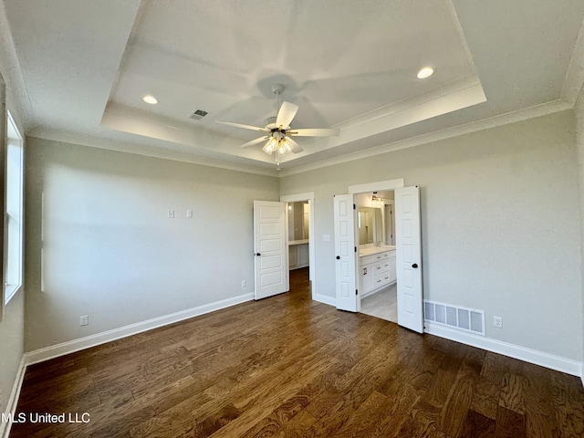 unfurnished bedroom featuring ceiling fan, a raised ceiling, ornamental molding, dark hardwood / wood-style floors, and ensuite bathroom