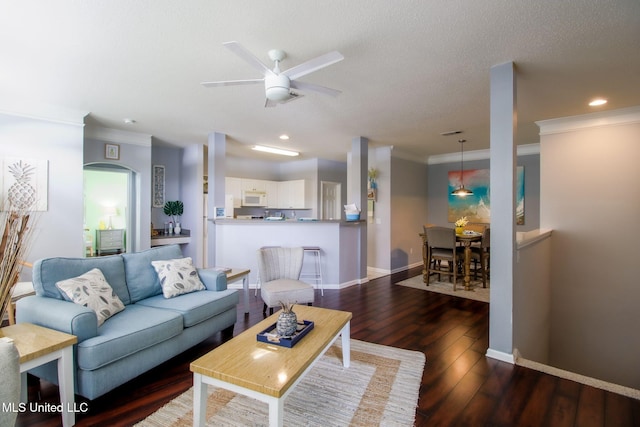 living room with a textured ceiling, dark wood-type flooring, ornamental molding, and ceiling fan