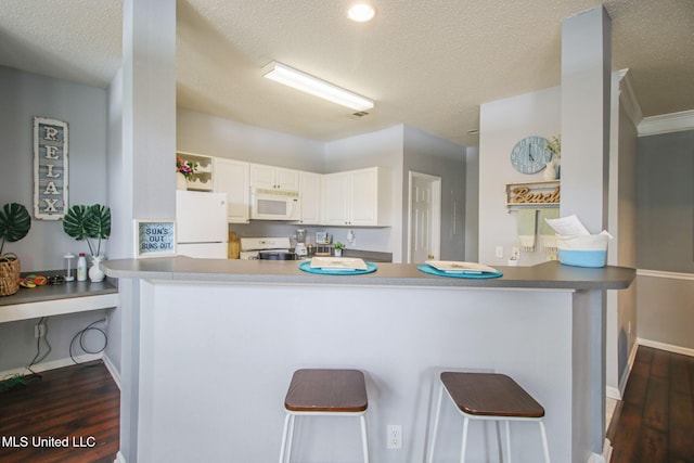 kitchen featuring dark wood-type flooring, a kitchen bar, kitchen peninsula, white appliances, and white cabinets