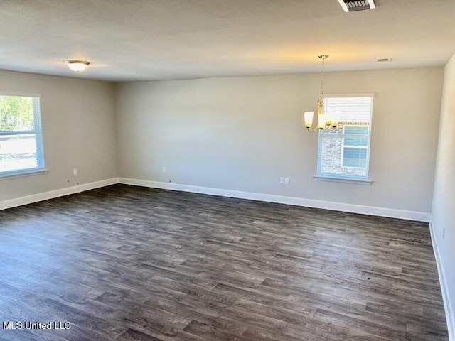 spare room with dark wood finished floors, visible vents, baseboards, and a chandelier