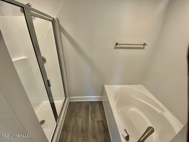 full bath featuring a bath, a stall shower, baseboards, and wood finished floors