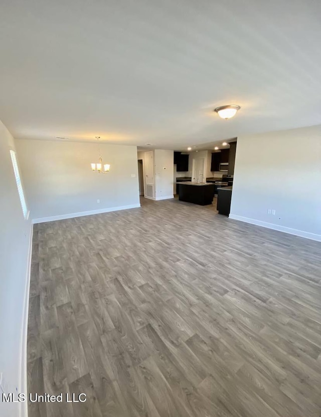 unfurnished living room with baseboards, wood finished floors, and a chandelier